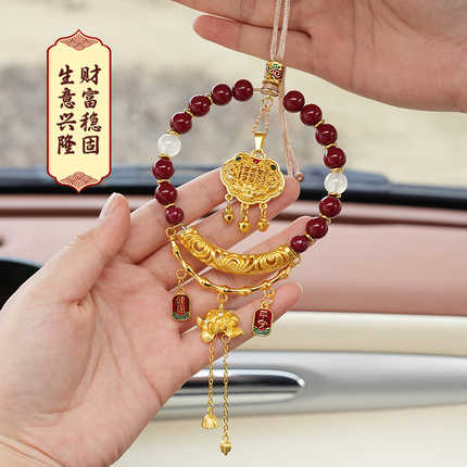 A hand holds an ornate ancient chinese cinnabar car pendant, featuring red beads, gold accents, and a decorative charm, perfe...