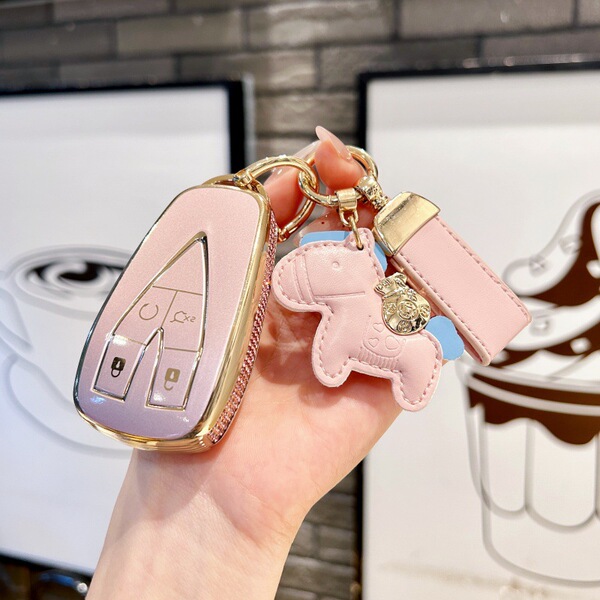 A hand holds a pink leather key cover for the changan cs75 plus, featuring gold accents and a cute horse-shaped keychain. the...