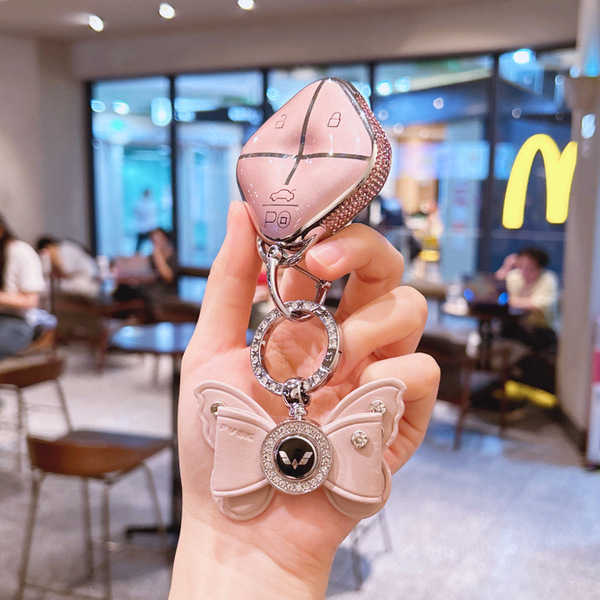 A hand holds a stylish wuling binguo key cover mini, featuring a slim silicone design with a decorative butterfly charm and c...