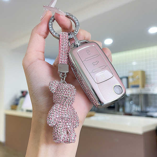 A hand holds a pink volkswagen key cover for bora, passat & tiguan l, adorned with a sparkling teddy bear charm and a glitter...