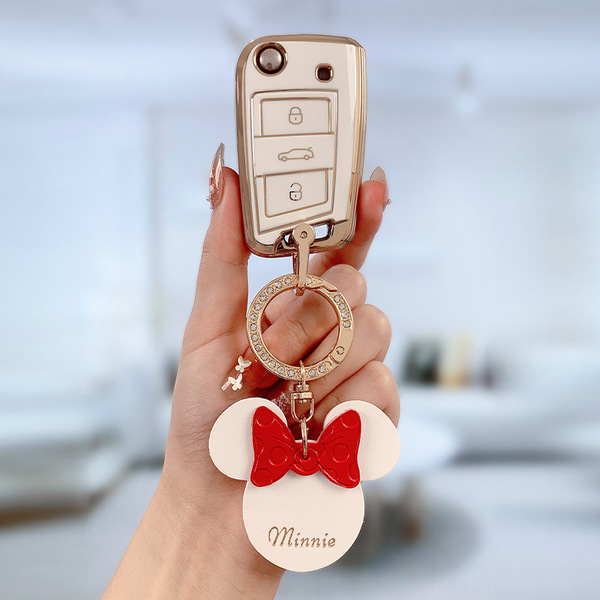 A hand holds a skoda key fob in a premium leather cover, featuring a minnie mouse charm with a red bow and minnie text, set a...