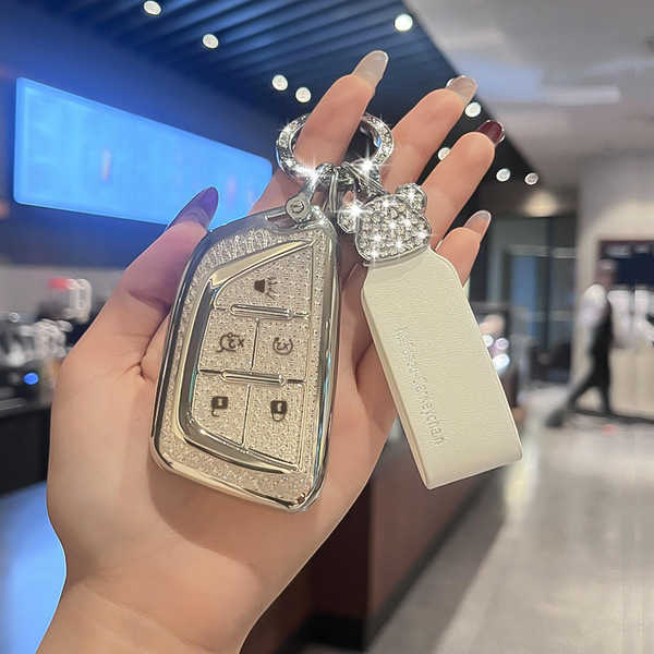 A hand holds a cadillac key cover with a sparkling design, featuring buttons for lock, unlock, and trunk release, paired with...
