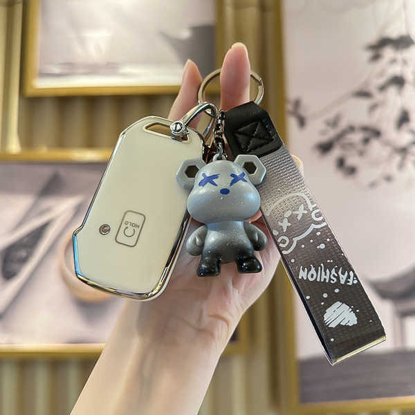A hand holds a sleek, white kia 5-button key cover with a stylish bear charm and a fashion strap, designed for models like k3...
