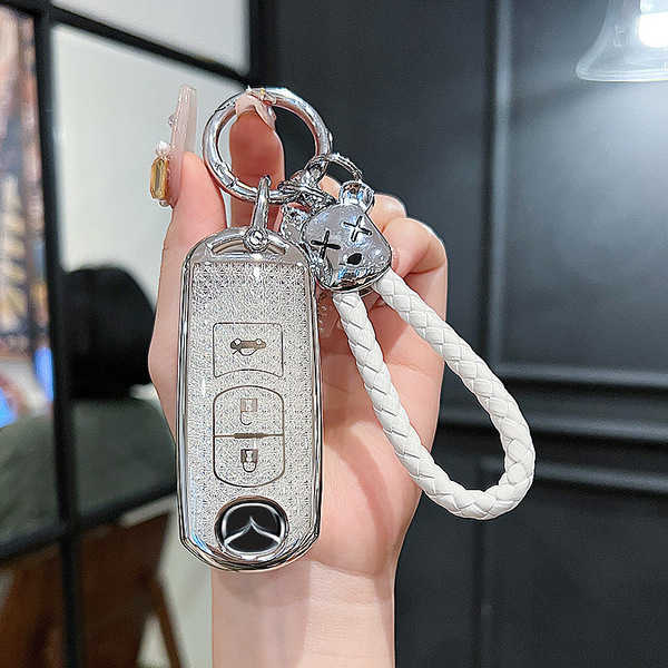 Elegant mazda key cover for cx-5, cx-30, mazda3, and cx-9, featuring a sleek silver design with a decorative charm and braide...