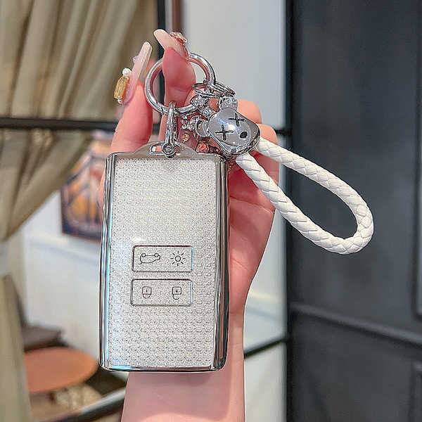 A hand holds a sleek, silver renault koleos key cover for 2022 models, featuring a textured design and a white braided lanyar...