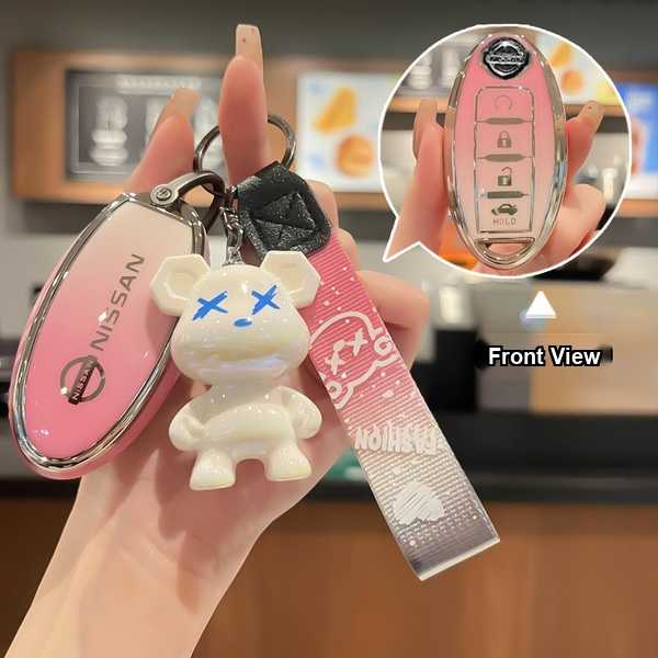 A hand holds a pink nissan alloy key cover with a cute white bear charm and a patterned strap, showcasing the front view of t...