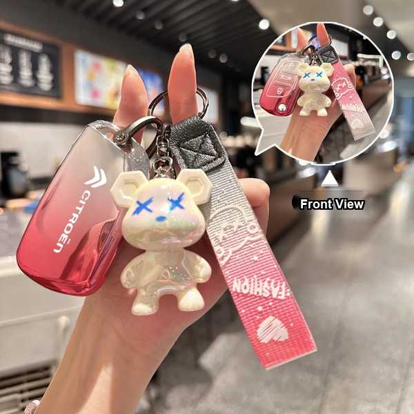 A hand holds a citroën key cover with a gradient red design and a cute bear keychain, featuring a fashion strap, shown in a f...