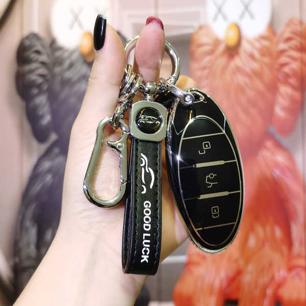A hand holds a sleek benteng t77 pro key cover, featuring a black leather strap with good luck text and a metallic car emblem...