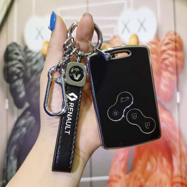 A hand holds a sleek black renault key cover for koleos, megane & talisman, featuring a carabiner and leather strap with the ...