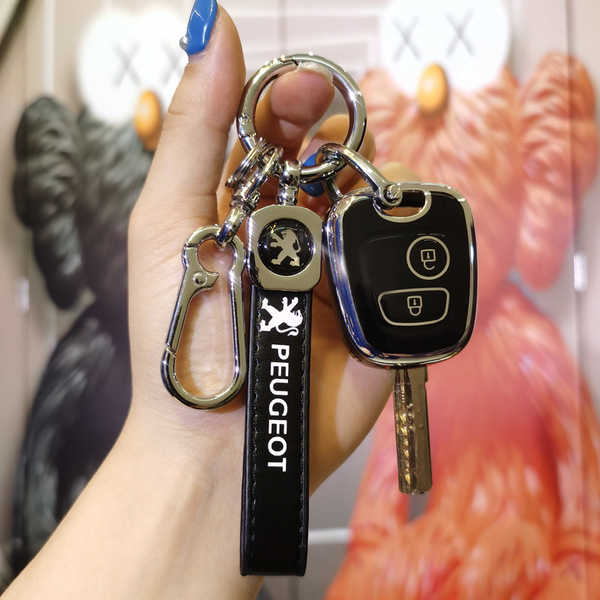 A hand holds a sleek peugeot key cover, featuring genuine leather and a slim fit design for 206/207/307 models, with a carabi...