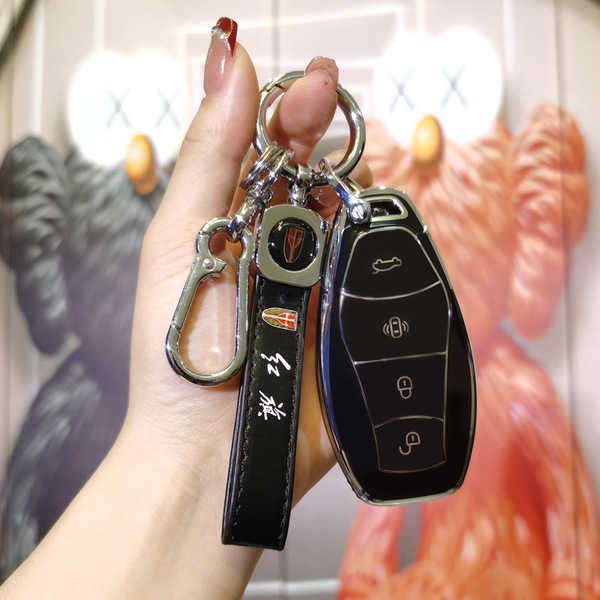 A hand holds a sleek black key cover for the 2023 hongqi h5 & hq9, featuring a leather strap with text and a carabiner, se...
