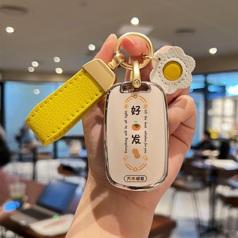 A hand holds a stylish wuling mini ev car key cover with a macaron shell design, featuring a yellow strap and a decorative fl...