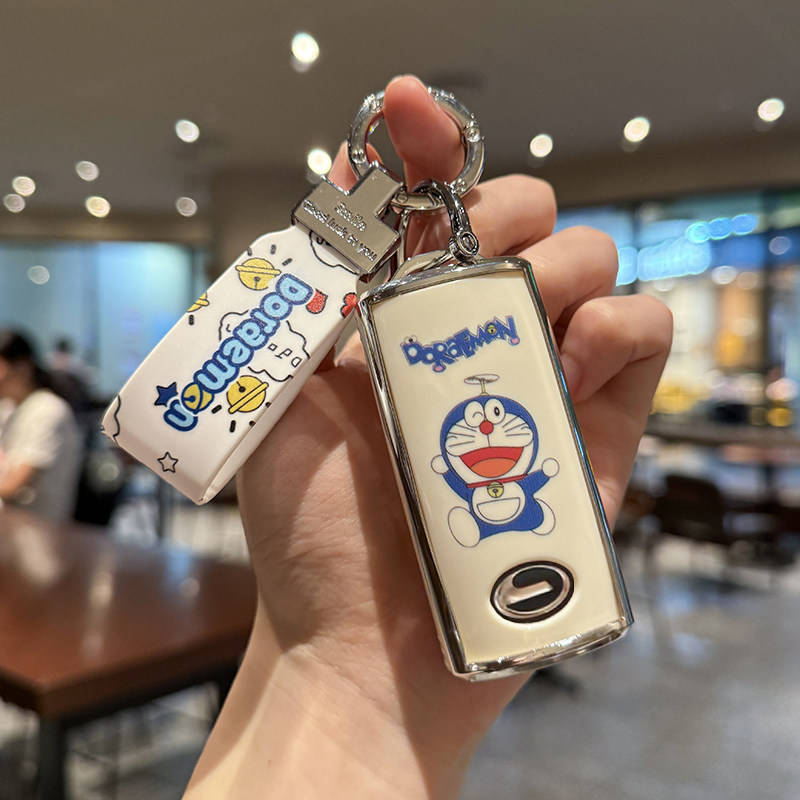 Hand holding a doraemon-themed key cover and strap for gac trumpchi vehicles, featuring a cartoon design on a sleek shell cas...