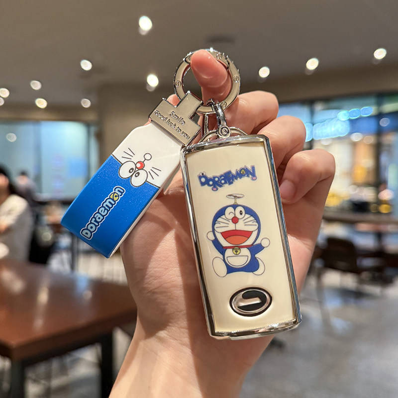 A hand holds a gac trumpchi gs4 plus key cover featuring a doraemon design, with a matching doraemon-themed keychain, set aga...