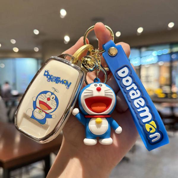 A hand holds a doraemon-themed key cover and matching keychain, featuring a cheerful doraemon design on a white case and a bl...