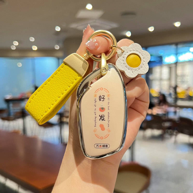 A hand holds a stylish roewe rx5 plus key cover with a yellow strap and flower charm, featuring all the best wishes for you t...