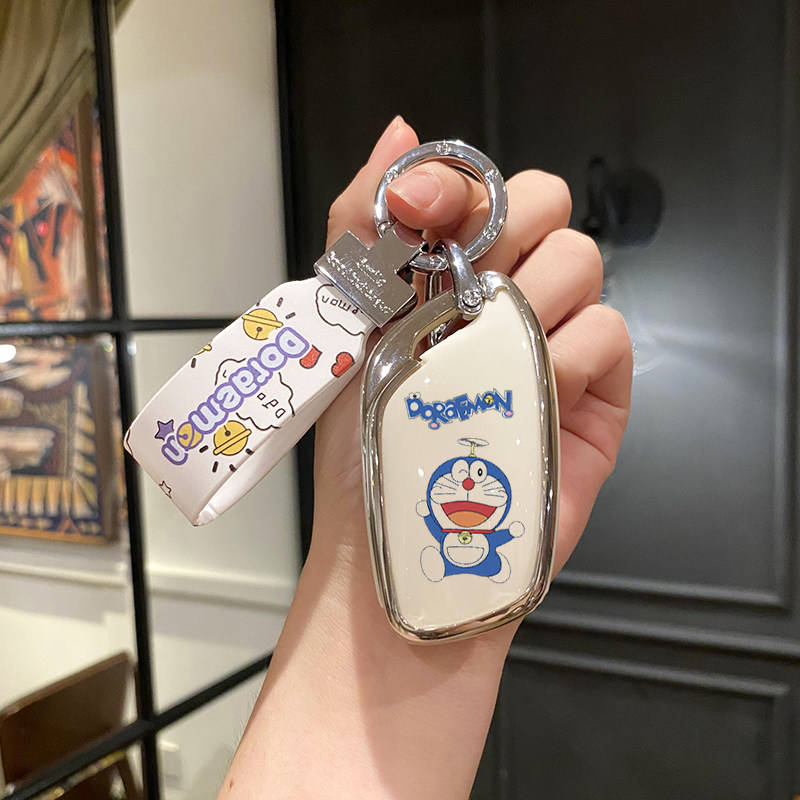 A hand holds a roewe rx5 plus car key cover featuring a cute doraemon design, paired with a matching doraemon-themed keychain...