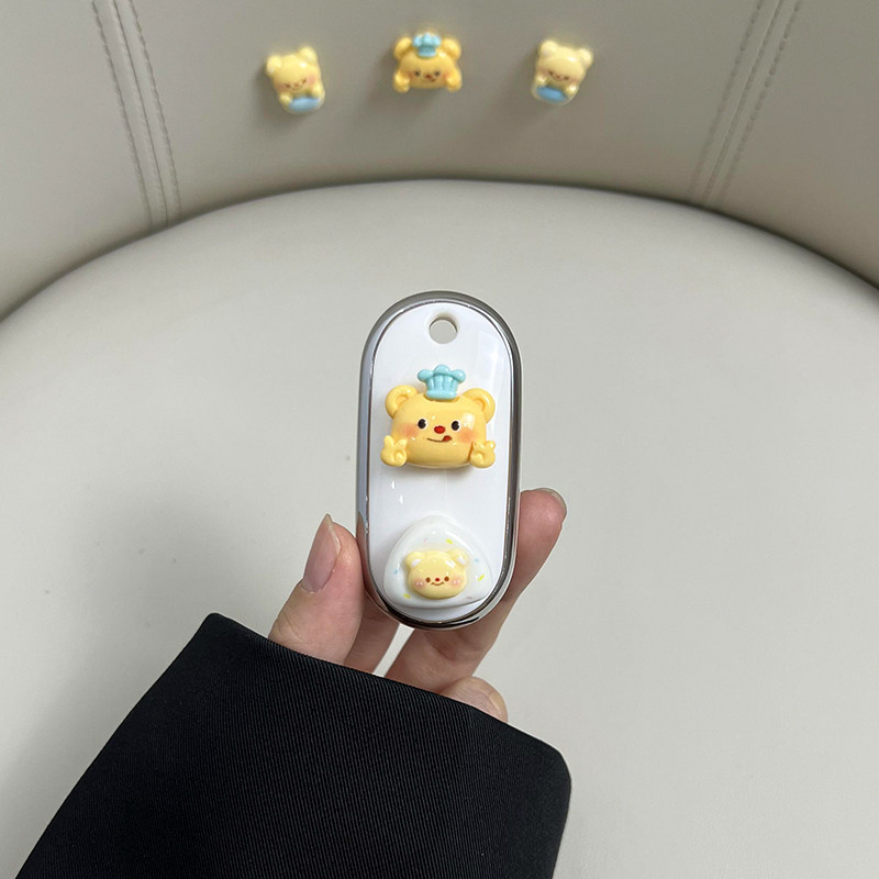 A hand holds a white yadea m5/e8/q6 car key cover featuring a cute yellow bear with a blue hat, matching the decorative bears...