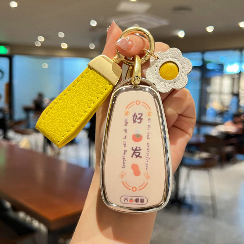 A hand holds a stylish changan cs75 plus car key shell case with a design, featuring a yellow strap and a white flower cha...