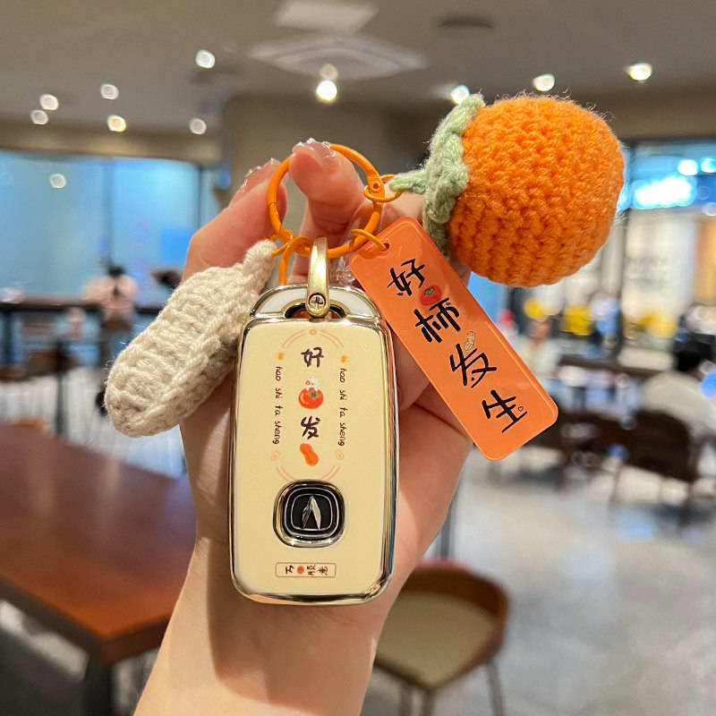A hand holds a changan cs75 plus car key shell case, featuring a matte black finish with a decorative orange knitted tag and ...