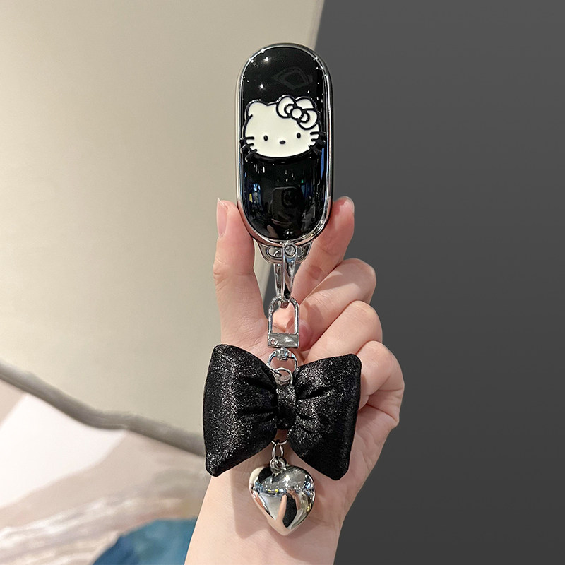 A hand holds a sleek black key cover featuring a white hello kitty design, adorned with a shiny black bow and a silver heart ...