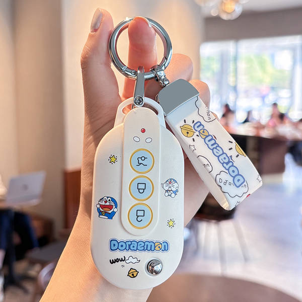 A hand holds a white wuling hongguang mini ev car key cover featuring doraemon designs, including buttons and playful graphic...
