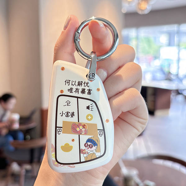 A hand holds a white buick regal car key cover featuring a playful design with chinese text and cartoon illustratio...