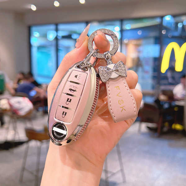 A hand holds a stylish pink nissan key cover with a bow and sky charm, designed for 14th-gen sylphy, altima, x-trail, and mor...