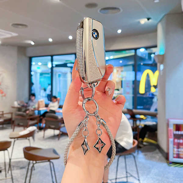 A hand holds a bmw key cover adorned with sparkling crystals and a decorative keychain, showcasing its elegant design for mod...