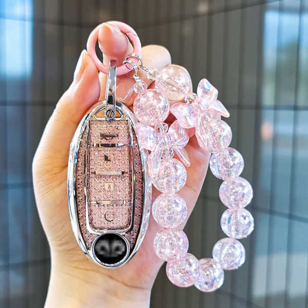 A hand holds a pink infiniti q50l key cover leather protector adorned with sparkling beads and a decorative charm, showcasing...