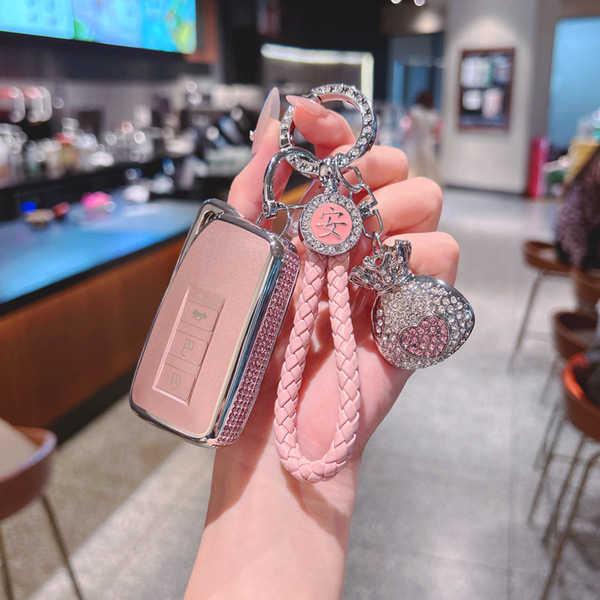 A hand holds a pink lexus nx260 key cover with a braided leather strap and a sparkling charm, showcasing its elegant design...