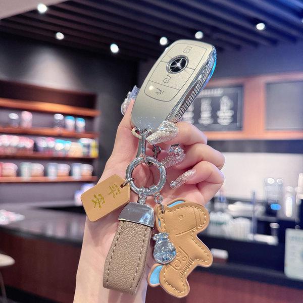 A hand holds a mercedes-benz key fob adorned with a stylish wax leather cover, featuring a bear-shaped charm and elegant acce...