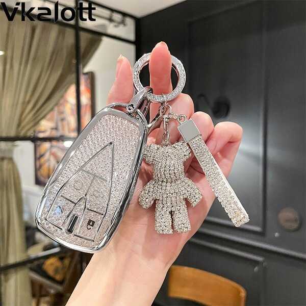 A hand holds a sparkling, rhinestone-encrusted key cover for the changan cs75 plus, featuring a decorative teddy bear charm a...