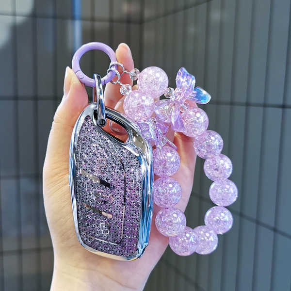 A hand holds a stylish mg5 key cover adorned with sparkling purple beads and a decorative charm, perfect for scorpio zodiac e...