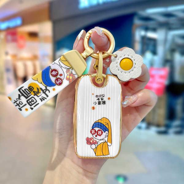 A hand holds a stylish mg rx5 plus key cover featuring a cartoon character in a yellow outfit, paired with a decorative flowe...