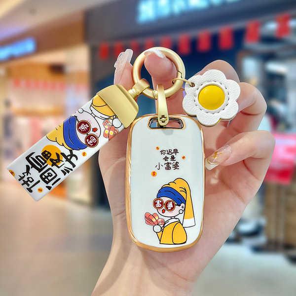 A hand holds a stylish baojun 510 key cover featuring a cartoon design with chinese text, paired with a matching keychain and...