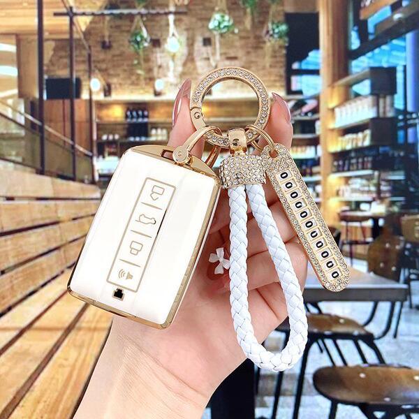 Elegant tank 300 key cover with gold accents and a braided white strap, showcased in a cozy cafe setting.