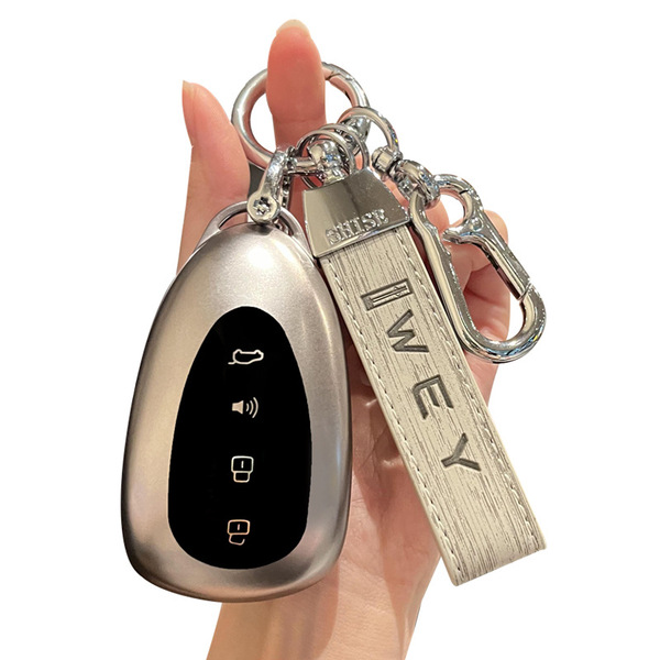 A hand holds a sleek, metallic key cover for the wey blue mountain, featuring a black panel with four buttons and a leather s...
