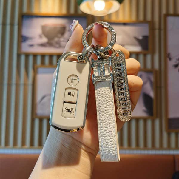 A hand holds a stylish ns125la motorcycle key cover, featuring a sleek white design with a leather strap and a decorative key...