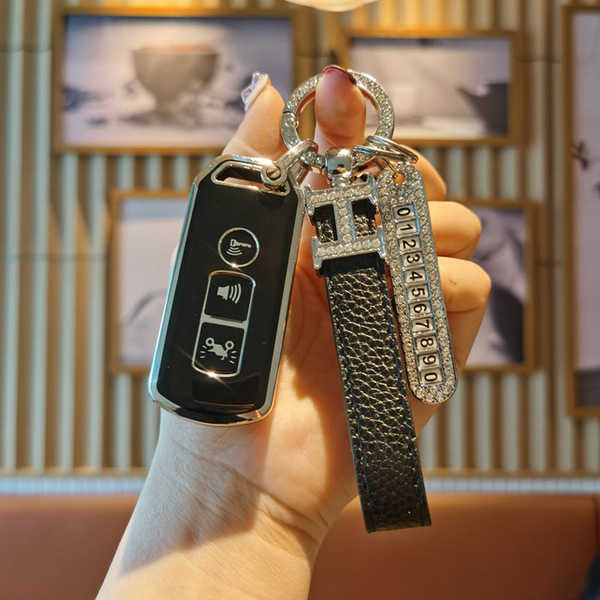 A hand holds a sleek black ns125la motorcycle key cover, featuring a textured leather strap and a decorative keychain with a ...