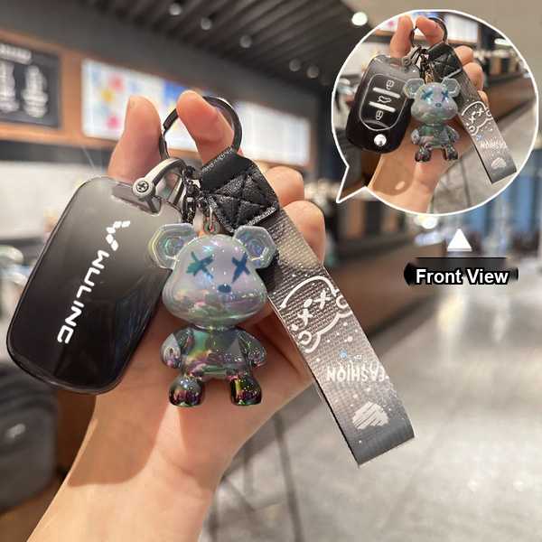 A hand holds a wuling hongguang mini key cover with a soft tpu anti-scratch design, featuring a shiny bear charm and a stylis...