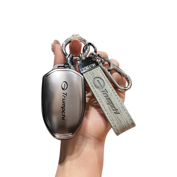 A hand holds a sleek, metallic gac trumpchi key cover with a leather strap, designed for models like gs4, gs5, and ga6. the c...
