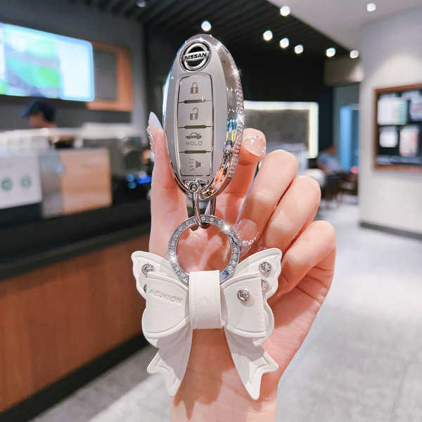 A hand holds a nissan key fob with a decorative white butterfly keychain, showcasing a stylish cover for altima, qashqai, syl...