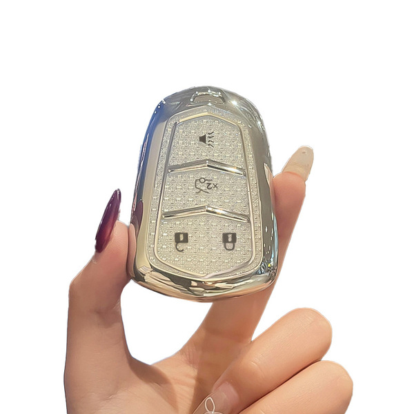 A hand holds a sleek, metallic cadillac key cover designed for models like the xt5, xt4, and ct5, featuring a textured finish...