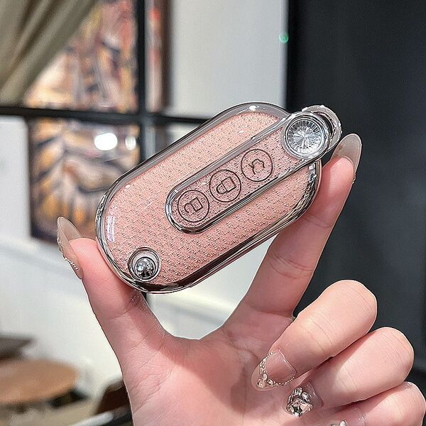 A hand holds a pastel pink wuling hongguang mini ev key cover with a textured finish and silver accents, featuring a sleek ga...