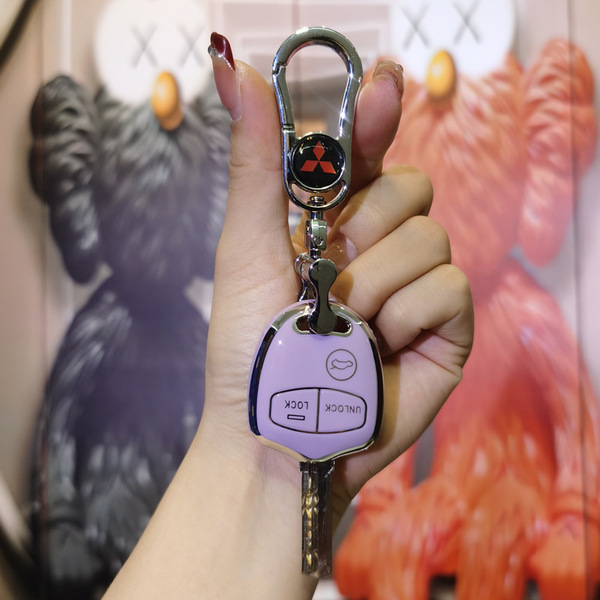 A hand holds a mitsubishi key fob with a purple cover, featuring lock and unlock buttons, against a backdrop of colorful art.
