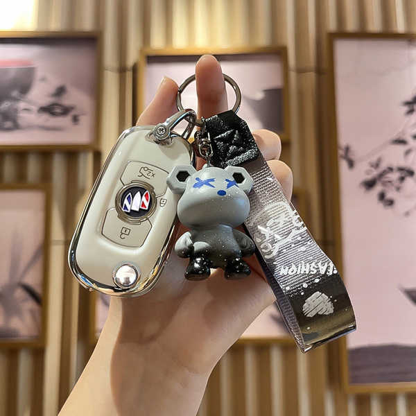 A hand holds a vinfast key cover for v3/v5/v7/v8, featuring a sleek white design with a silver accent and a cute gray bear ch...