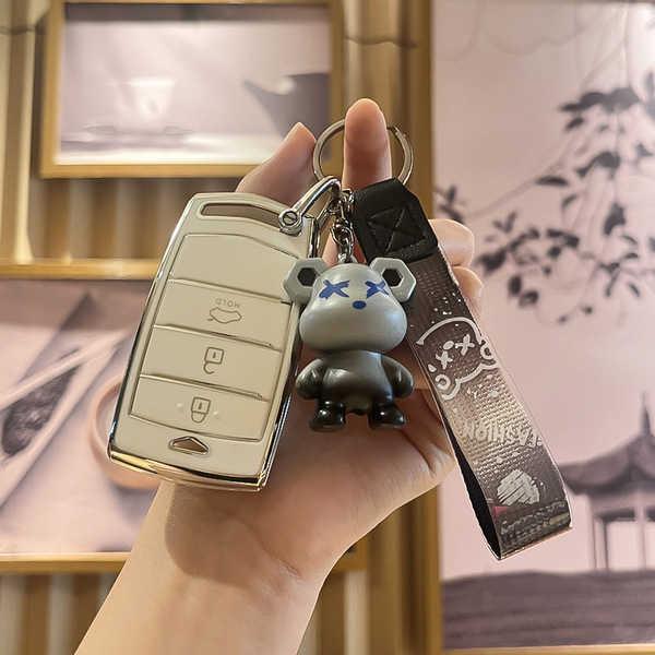 A hand holds a genesis g90 key cover with a sleek design, featuring a cute bear charm and a stylish leather strap, perfect fo...