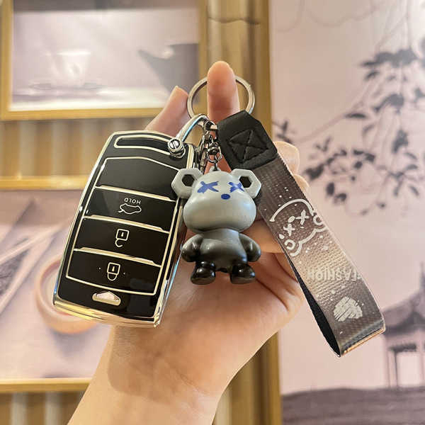 A hand holds a sleek black genesis g90 key cover with a stylish bear charm and wrist strap, showcasing its premium leather de...