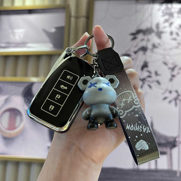 A hand holds a sleek black lexus smart key cover with a metallic finish, featuring a cute bear-shaped keychain and a matching...